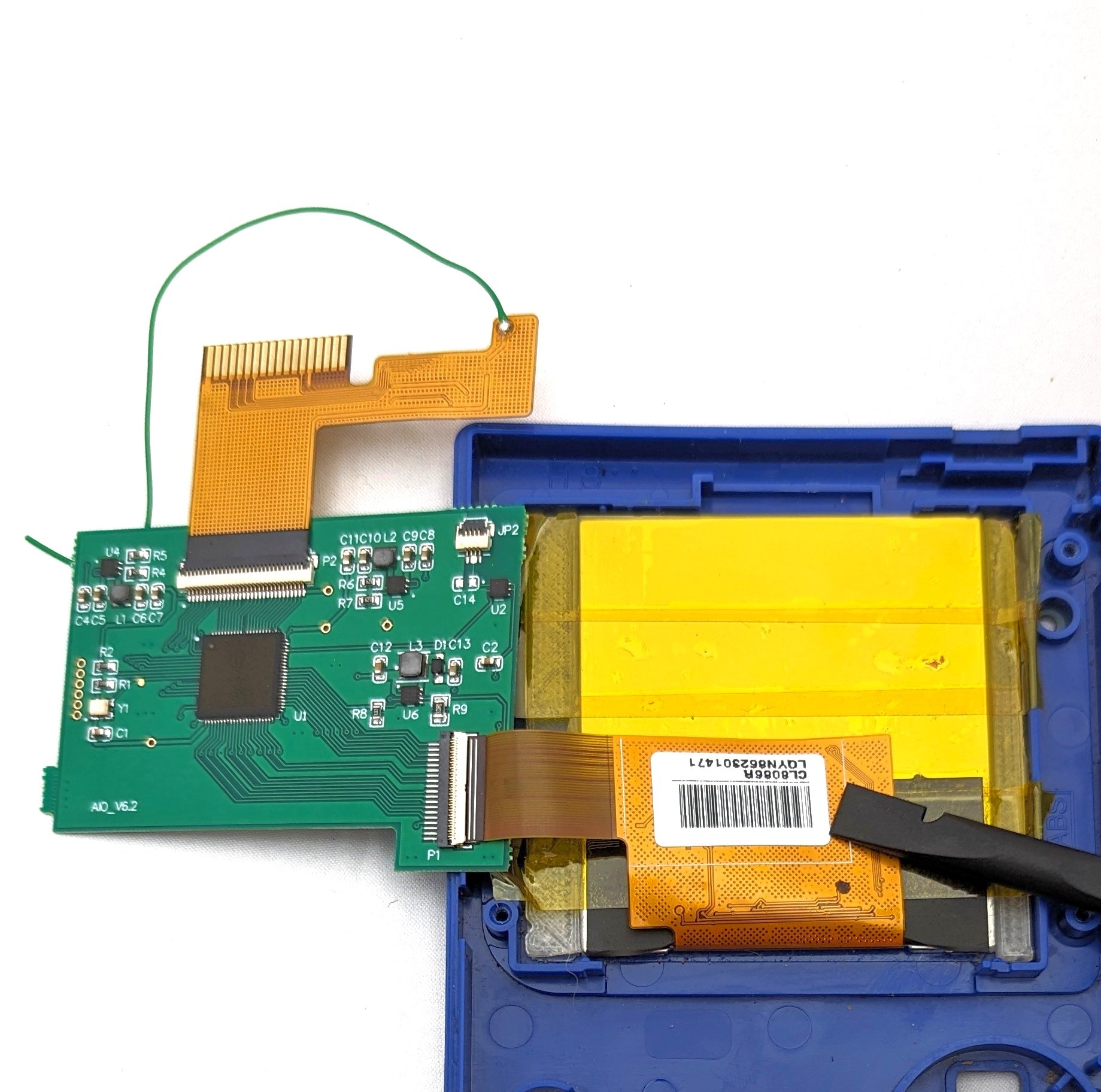The inside shell of a game boy with a new screen implemented. A circuit board hangs off the side with a single wire leading off.