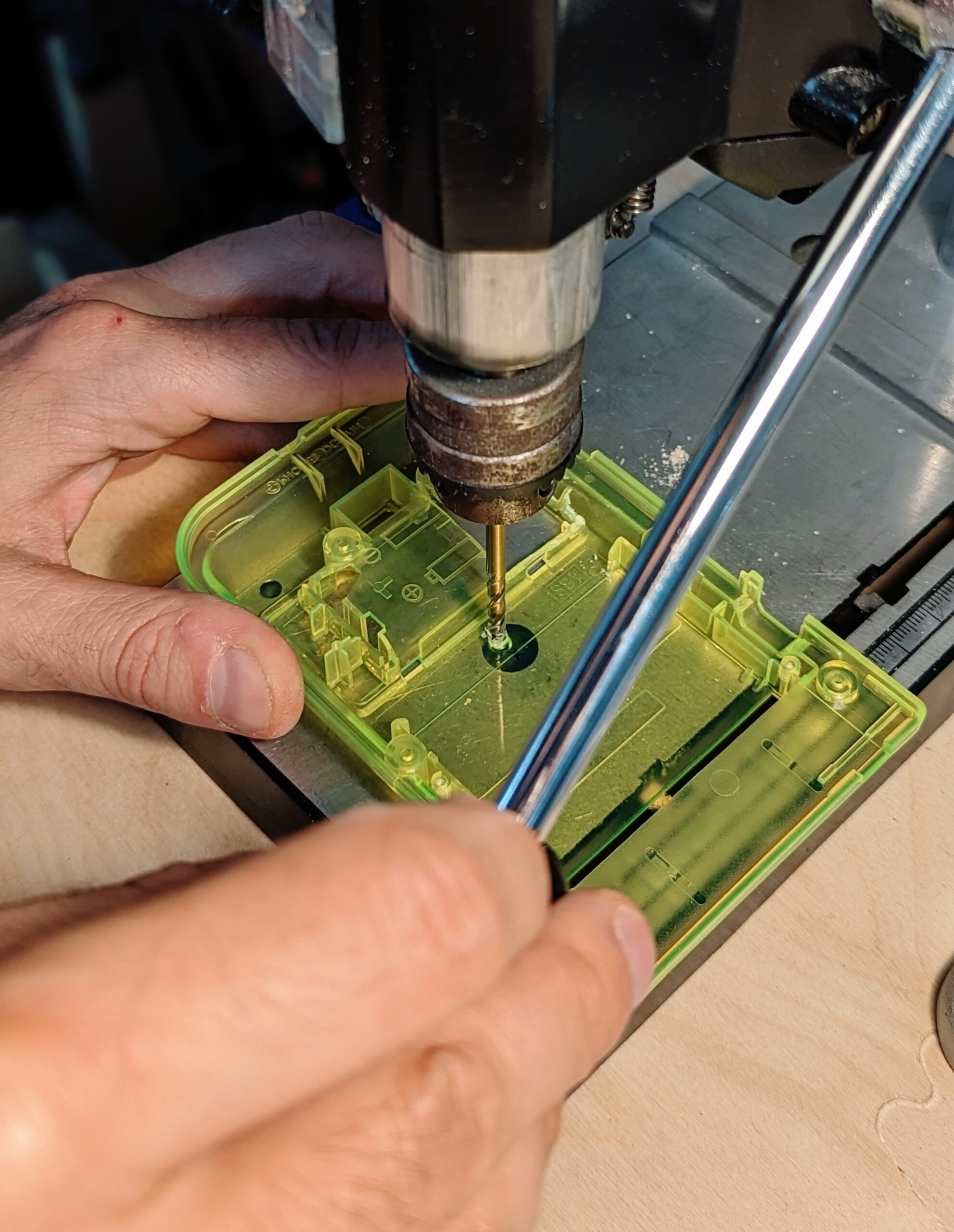 a game boy pocket shell is held under a drill press, which has just drilled a hole through it