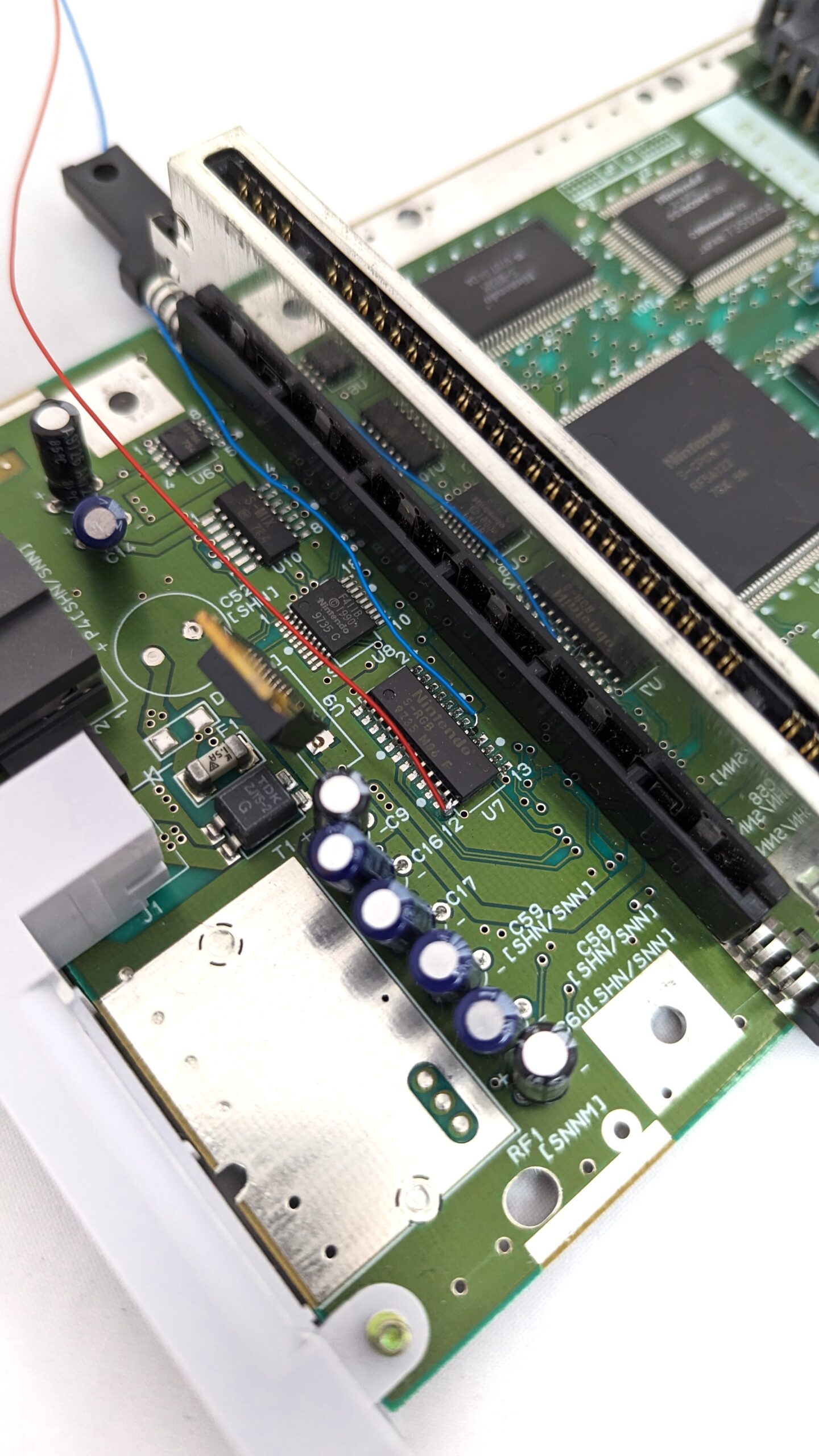 An inside view of a SNES with a red wire sticking out of a chip